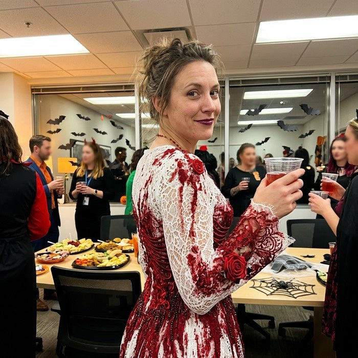 Woman in a blood-splattered white dress at an office Halloween party