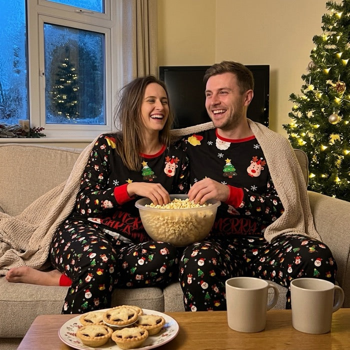 Couple en pyjamas assortis noirs à motif Père Noël, sur le canapé le soir du réveillon